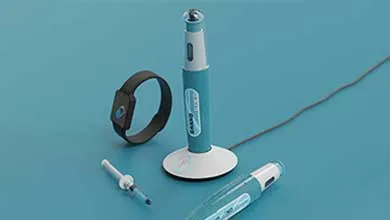 Medical devices on a blue surface: a teal and white electronic pen on a charging stand, a black wristband, a syringe, and another pen.