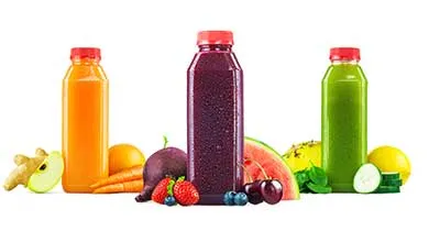 Three juice bottles, colored orange, purple, and green, are arranged in a row. They are surrounded by fresh carrots, beets, berries, and cucumbers on a white background.