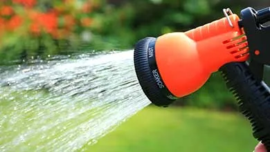 Orange and black nozzle spraying a stream of water onto a green lawn.