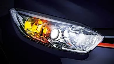 Close-up of a modern car’s headlight on a dark vehicle, showing the white headlamp and yellow indicator light both lit.