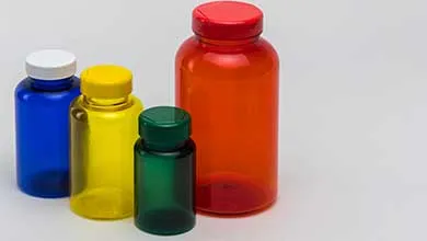 Four plastic pill bottles in blue, yellow, dark green, and orange are arranged on a gray background.
