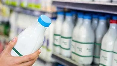 Person holding a plastic milk bottle while scanning product information on a smartphone in a grocery aisle.