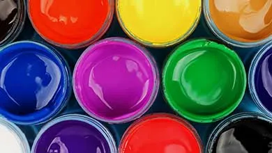 Overhead close-up of several open paint pots filled with glossy red, yellow, blue, magenta, and green paint.