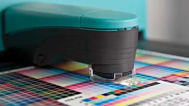 Close-up of a teal and black spectrophotometer scanning a grid of colored squares on a printed chart.