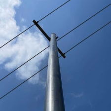 Low-angle view of a composite utility pole with three power lines against a blue sky with white clouds